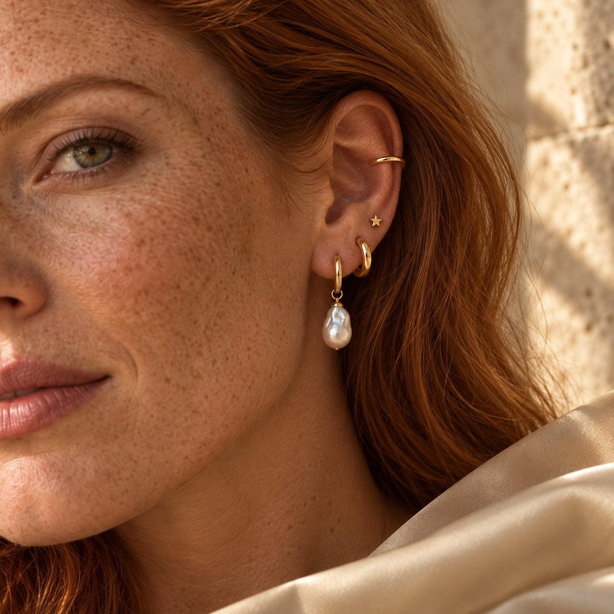 Oreille ornée d'une créole, d'une puce étoile, d'un ear cuff et d'une perle baroque