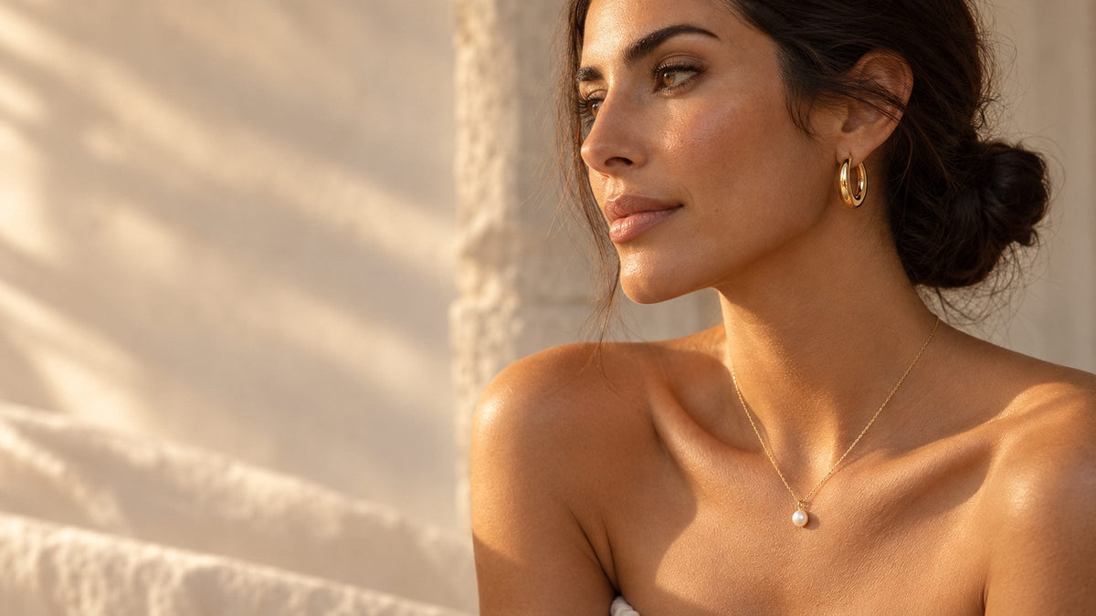 Profil d'une femme portant des créoles dorées et un collier à perle, dans la lumière du soir
